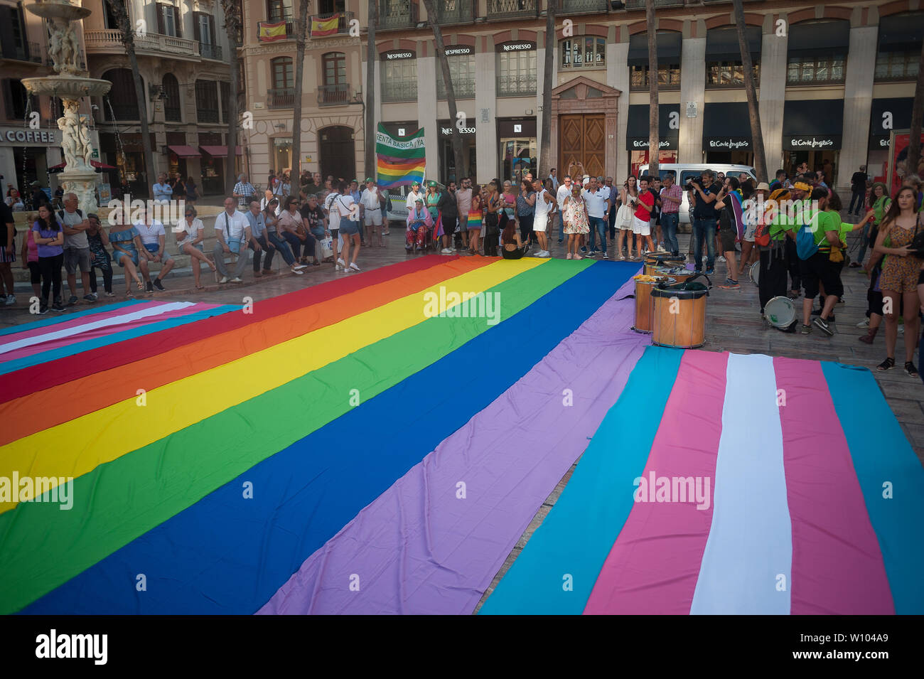 People gather around a large pride flag during a demonstration to celebrate the International Pride LGTBI Day 2019, organized by Andalusia Rainbow Federation.Thousands of people around the world take part on the Pride LGTBI, marked the anniversary of 50 years of Stonewall riot which commemorated the fight of gays, lesbians, transgender, bisexuals and intersexual during the first demonstrations in US in favour of their rights. Stock Photo
