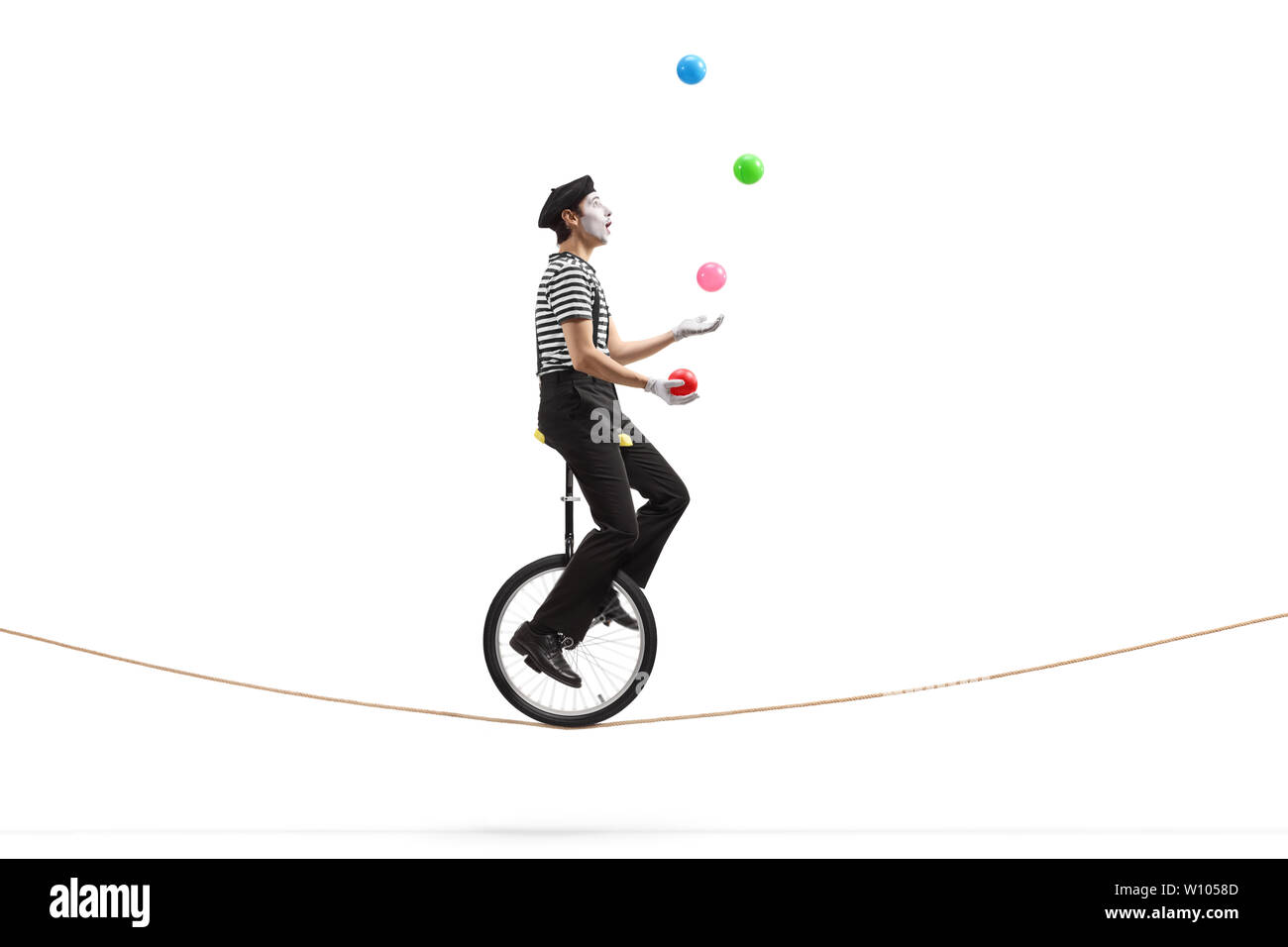 Full length profile shot of a mime riding a unicycle on a rope and ...