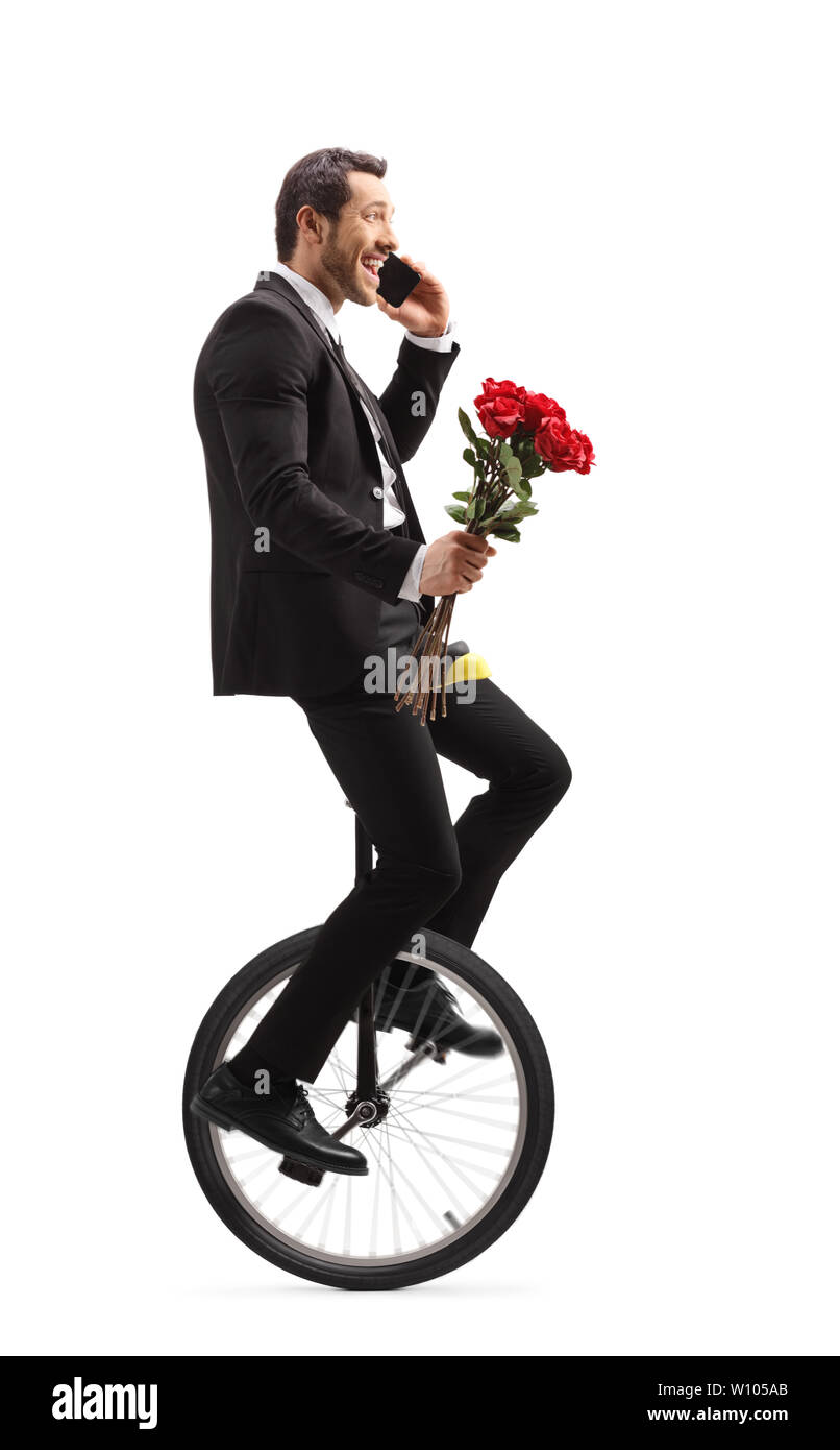 Full length shot of a businessman talking on a phone, riding a unicycle and carrying a bunch of red roses isolated on white background Stock Photo