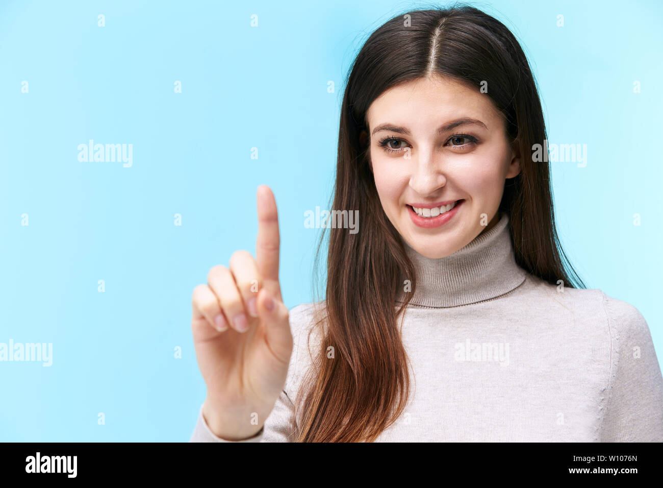 beautiful young caucasian woman pressing a virtual button, looking at camera smiling, isolated on blue background Stock Photo