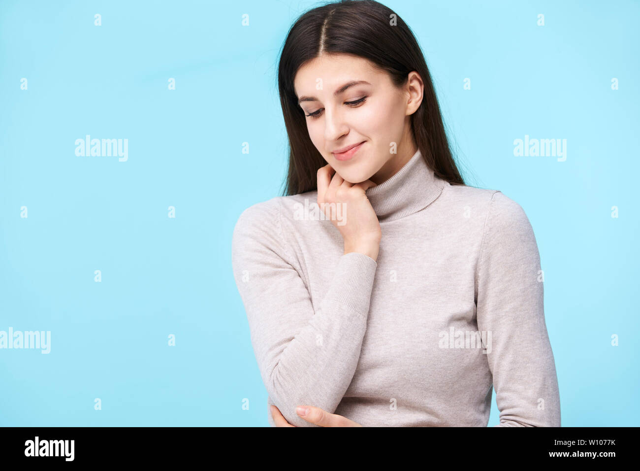 studio portrait of a beautful caucasian woman, looking down, smiling, isolated on blue background Stock Photo