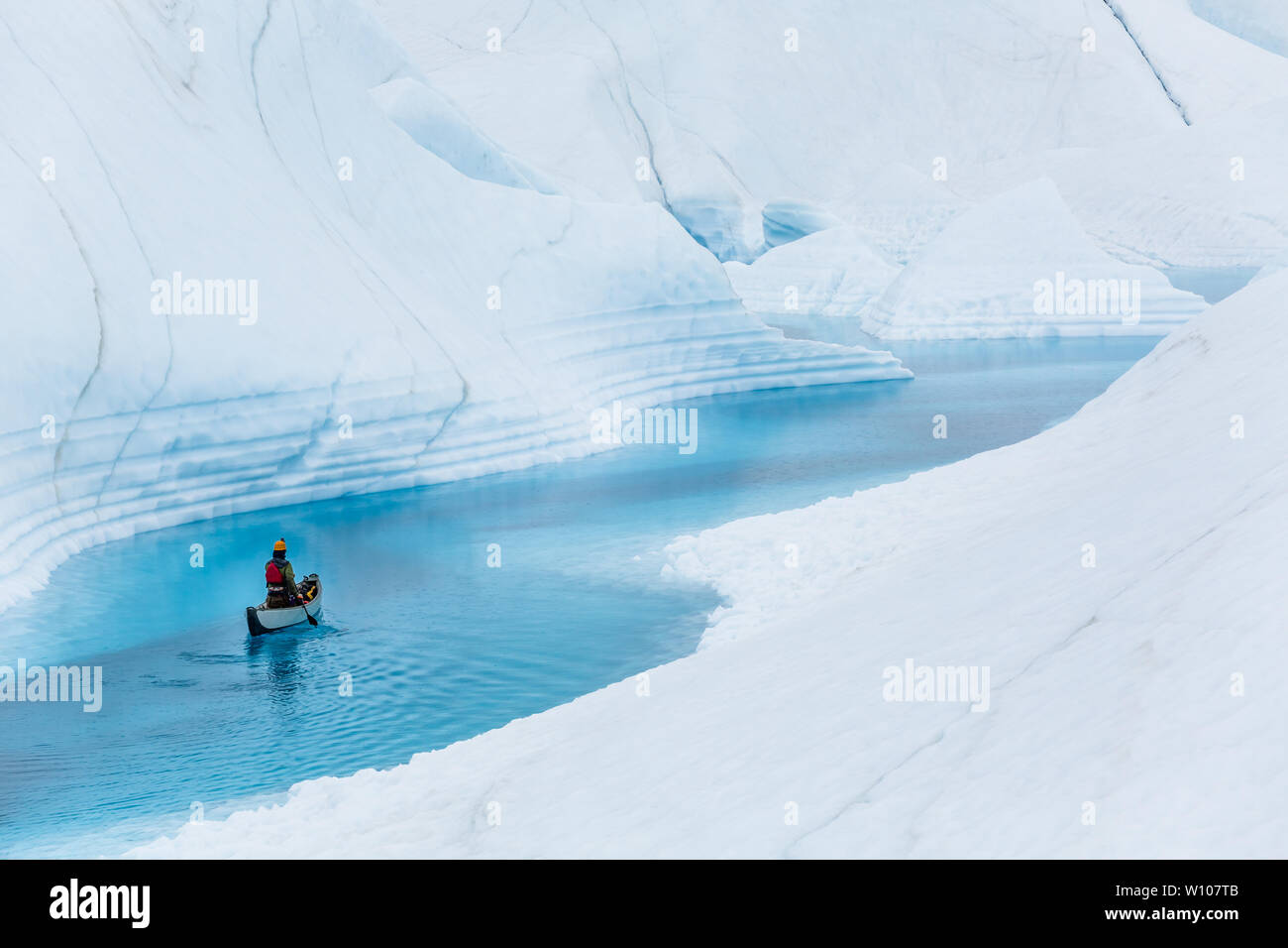 A man paddles solo on an inflatable canoe down a still water river on the Matanuska Glacier in the Alaskan wilderness. Stock Photo