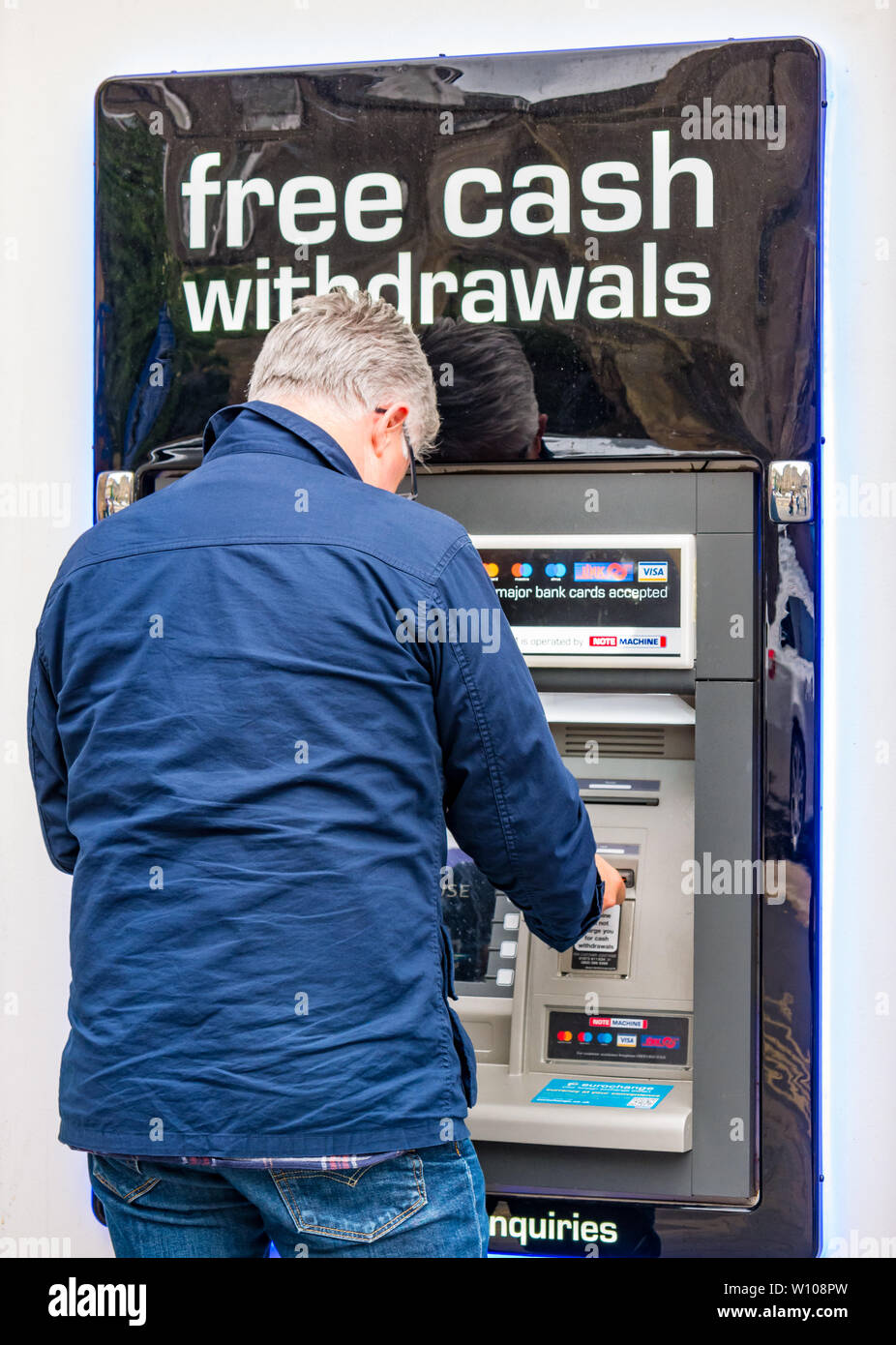 Mature man withdrawing cash from ATM automated teller hole in the wall machine, Scotland, UK Stock Photo