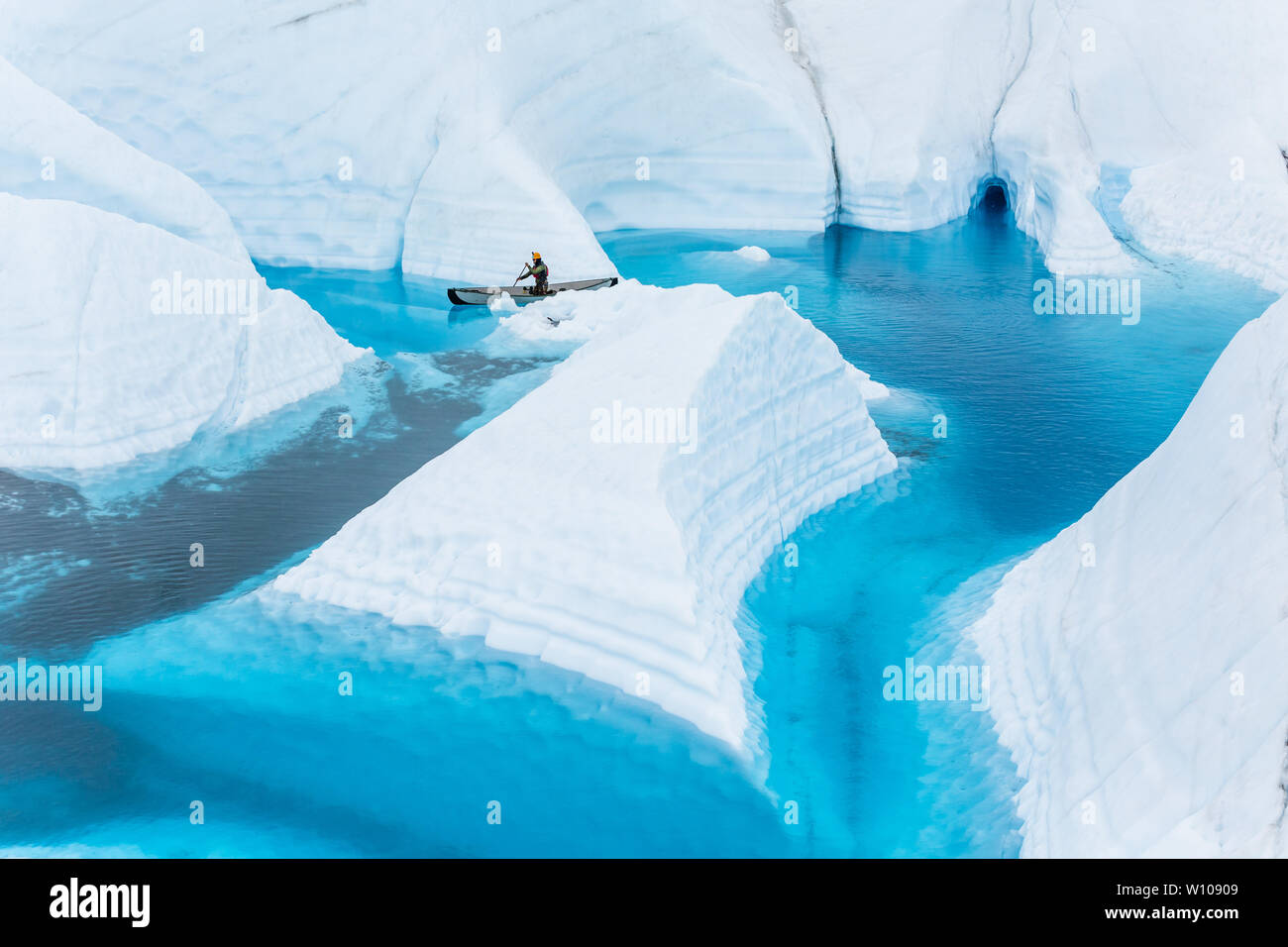A young man and ice climbing guide paddles through a narrow canyon behind a chunk of white glacier ice resembling an iceberg. This fin is only surroun Stock Photo