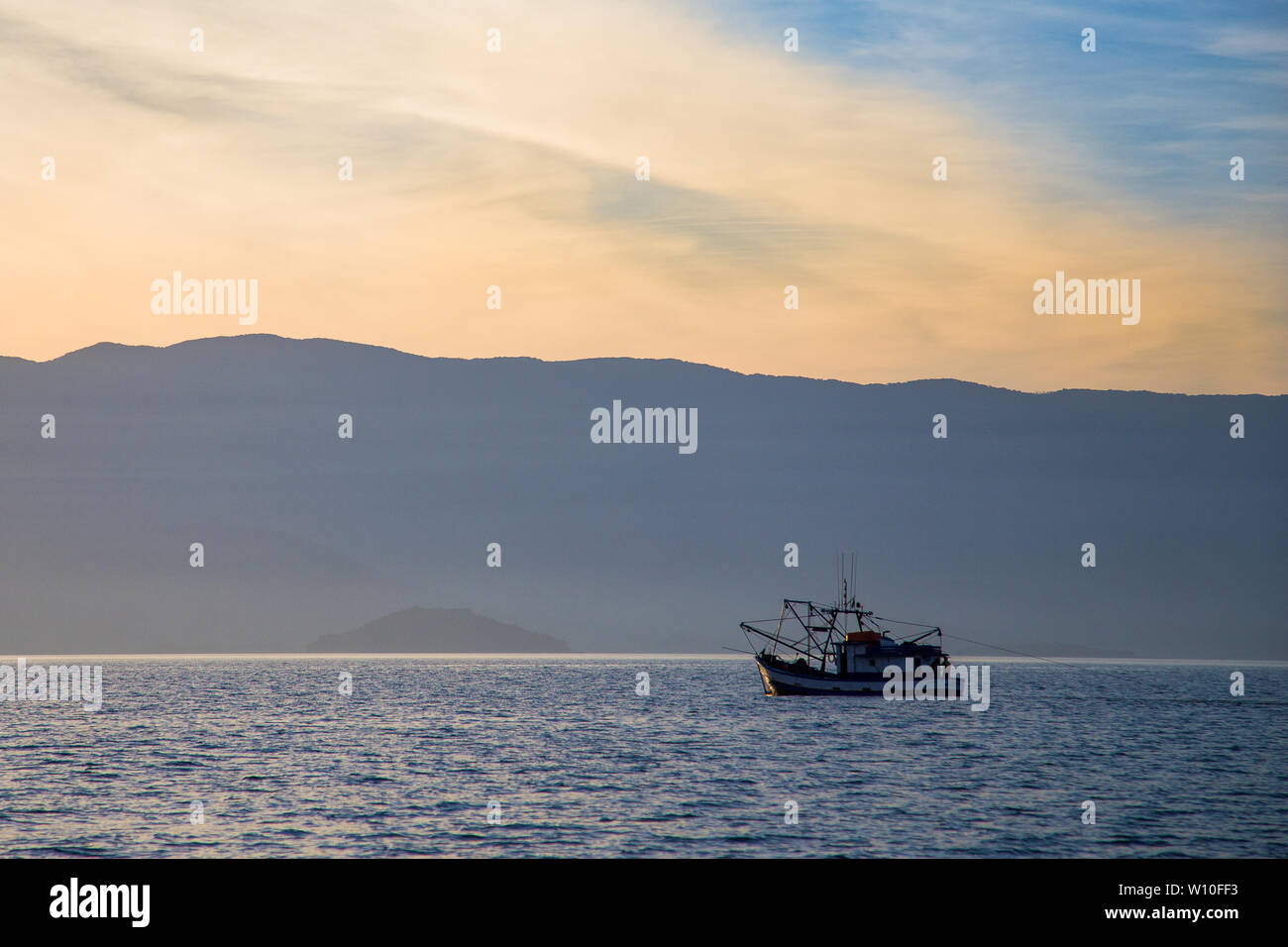 Solitary fishing boat navigating a generic sea with mountains skyline as background Stock Photo