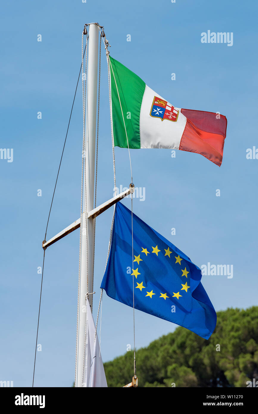 European and Italian flag with emblem of the four Maritime Republics, Venice, Genoa, Pisa and Amalfi hanging on a ship's mast on blue sky Stock Photo