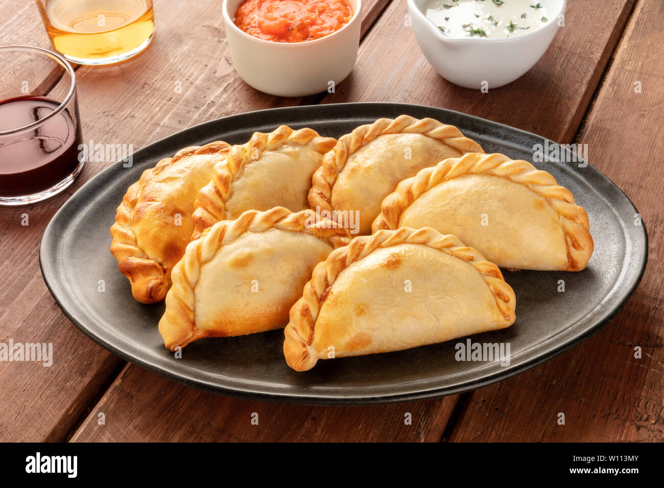 A closeup of Argentinian empanadas with sauces and wine on a dark rustic wooden background Stock Photo