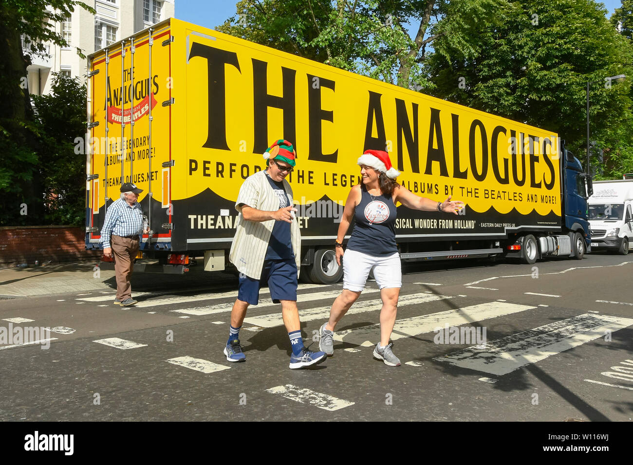 Abbey Road, London, UK.  29th June 2019.  UK Weather:  Tourists crossing the famous Abbey Road zebra crossing made famous by The Beatles in an elf and a santa hat on a scorching hot day in London.  A lorry is parked on the road which has advertising on it for 'The Analogues' Beatles musical.  Picture Credit: Graham Hunt Photography. Credit: Graham Hunt/Alamy Live News Stock Photo