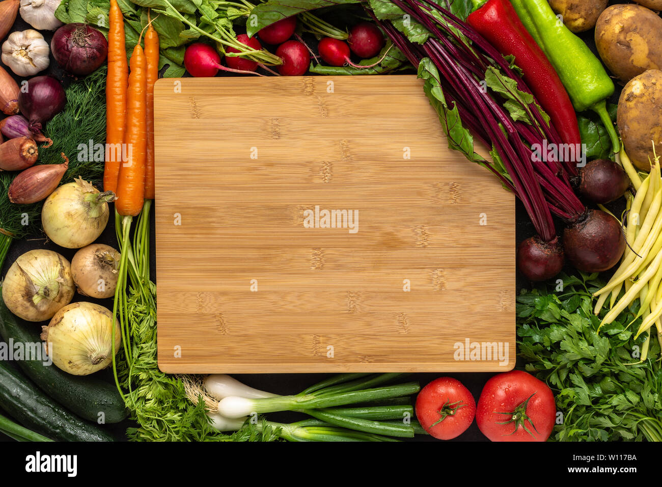 Empty Chopping Board with Fresh Vegetables Background. Healthy Eating Concept with Copy Space. Vegan Raw Food. Stock Photo