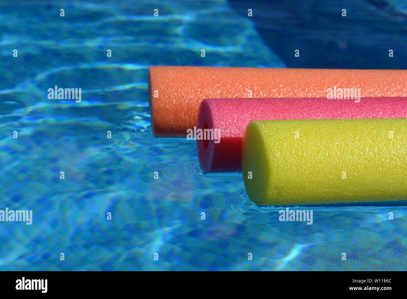 Brightly coloured pool noodles and swimming pool, with copy space. Fun