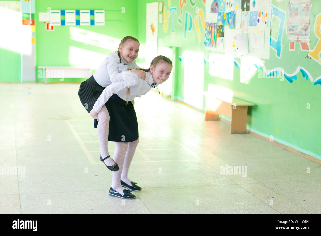 School friends at recess. A tall girl rolls her friend in her lap. Stock Photo