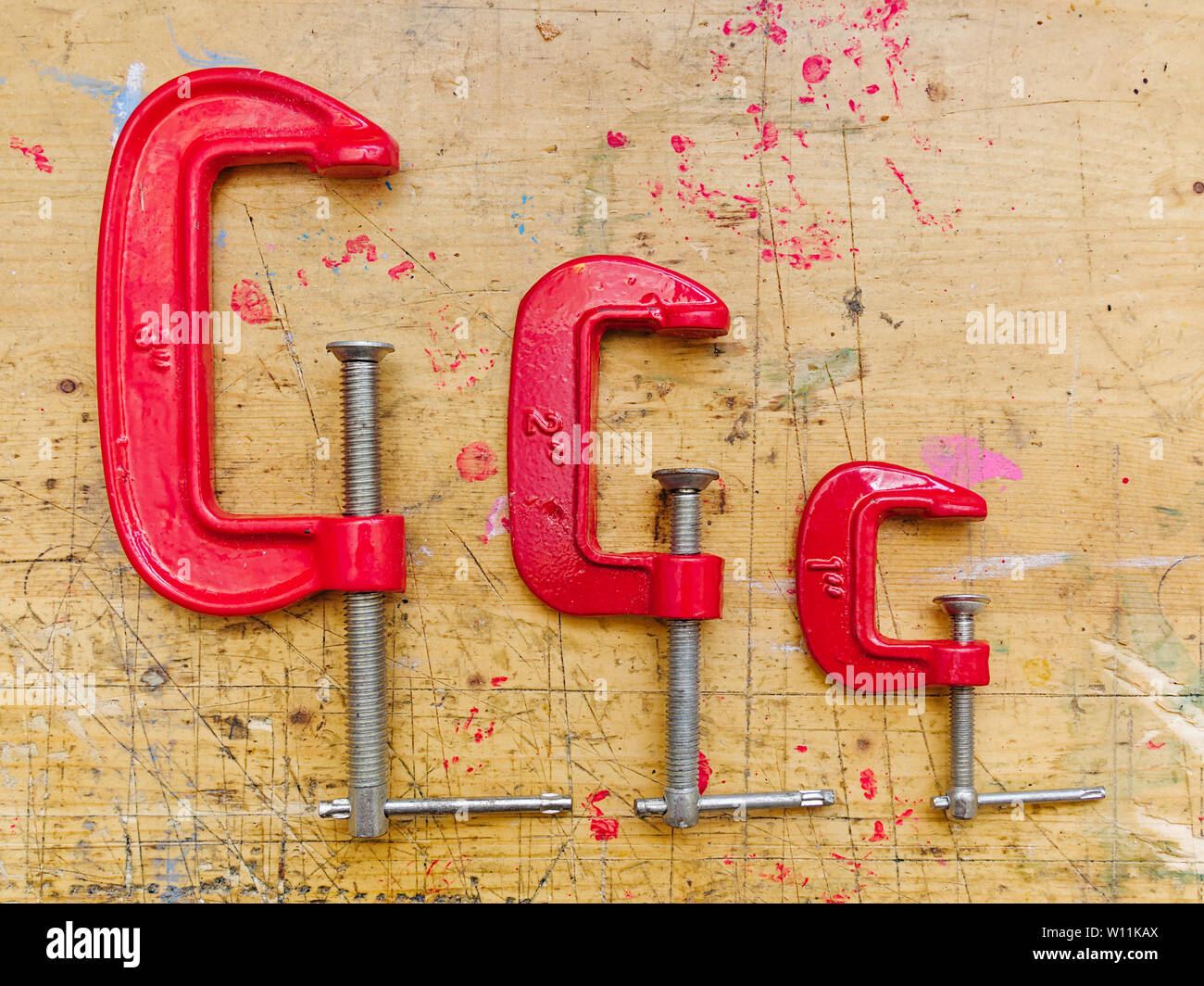 Set of three red  metal C clamps on wooden workbench surface background. Stock Photo