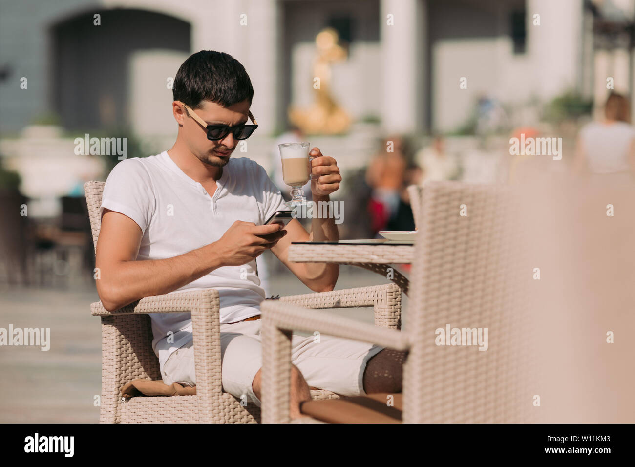 portrait of man in sunglasses sitting in a cafe and drinking coffee on a sunny summer day. Stock Photo