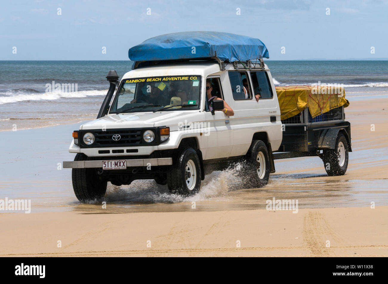 A tourist carrying 4WD towing a camper trailer along the wide sandy beach on the 75 mile long Sandy Highway on Fraser Island, Queensland, Australia  F Stock Photo