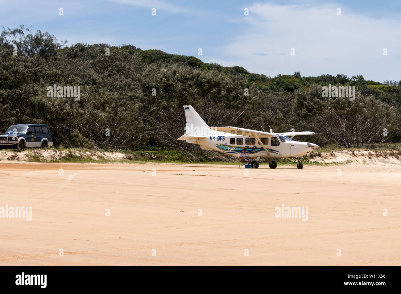 A pilot sitting under the wing of his small passenger carrying aircraft parked on the 75 mile beach on Fraser Island, Queensland, Australia.   The air Stock Photo