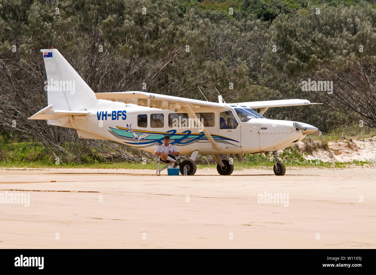 A pilot sitting under the wing of his small tourist passenger carrying aircraft, parked on the 75 mile  beach on Fraser Island in Queensland, Australi Stock Photo