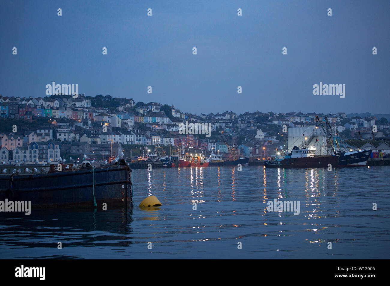 A view of Brixham and the houses overlooking the harbour with fishing vessels in the foreground in the evening in June. Brixham Devon England UK GB Stock Photo