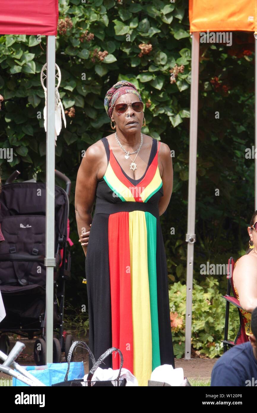 Liverpool, UK. 29th June, 2019. Black woman in a dress of Jamaican colours celebrating Liverpool's Windrush generation at a community family fun day event in Faulkner Square Park, Toxteth, Liverpool with performances Liverpool, UK. 29th June, 2019. Black woman in a dress of Jamaican colours celebrating Liverpool's Windrush generation at a community family fun day event in Faulkner Square Park, Toxteth, Liverpool with performances