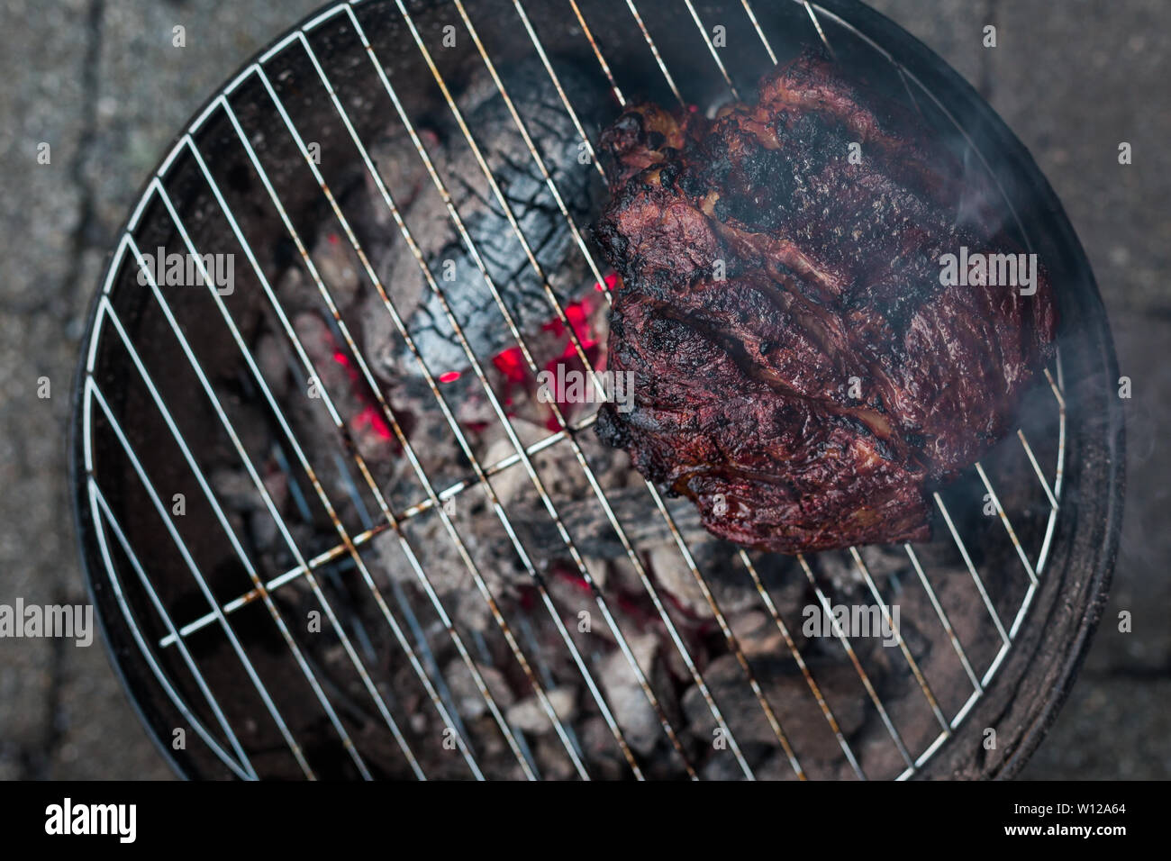 A top down view of a large beef brisket and being barbequed on a small  charcoal hibachi grill with glowing coals underneath Stock Photo - Alamy