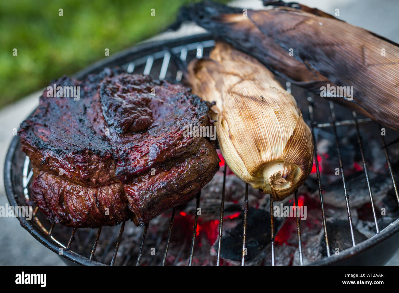 A large beef brisket and corn in the husk being barbequed on a small