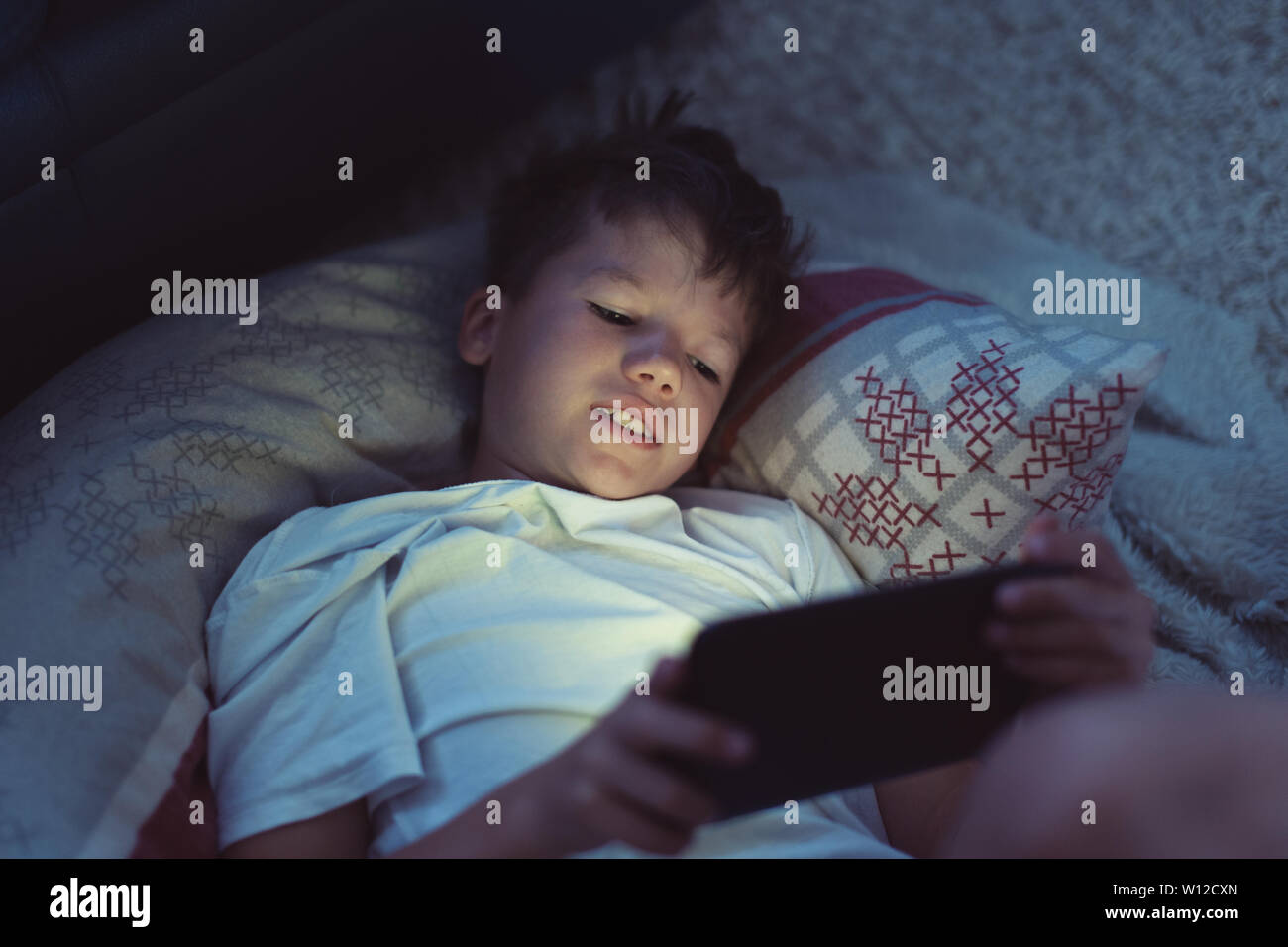 Little boy playing on digital tablet at night in bedroom Stock Photo