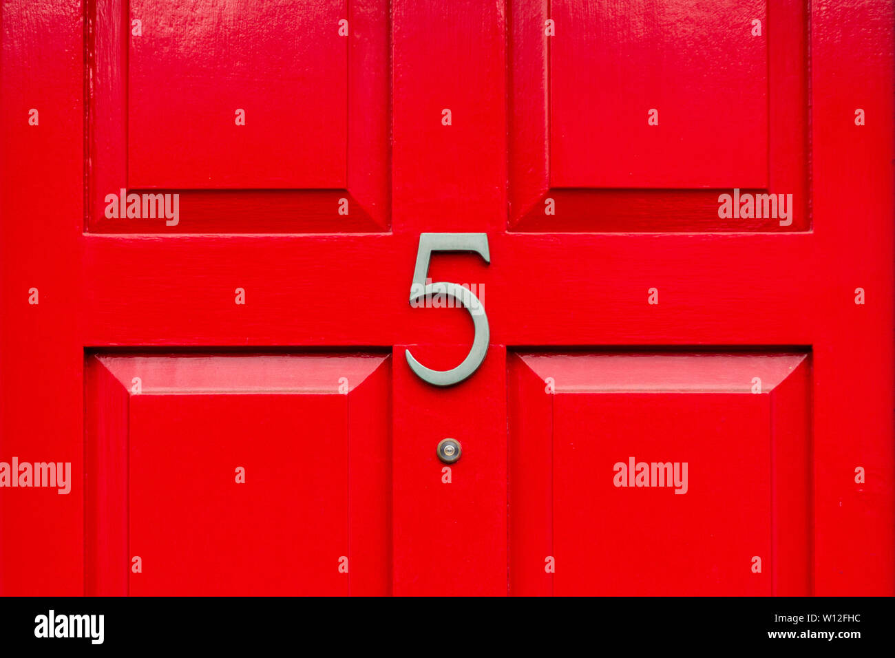 House number five with the 5 in bronze on a bright red wooden front door Stock Photo