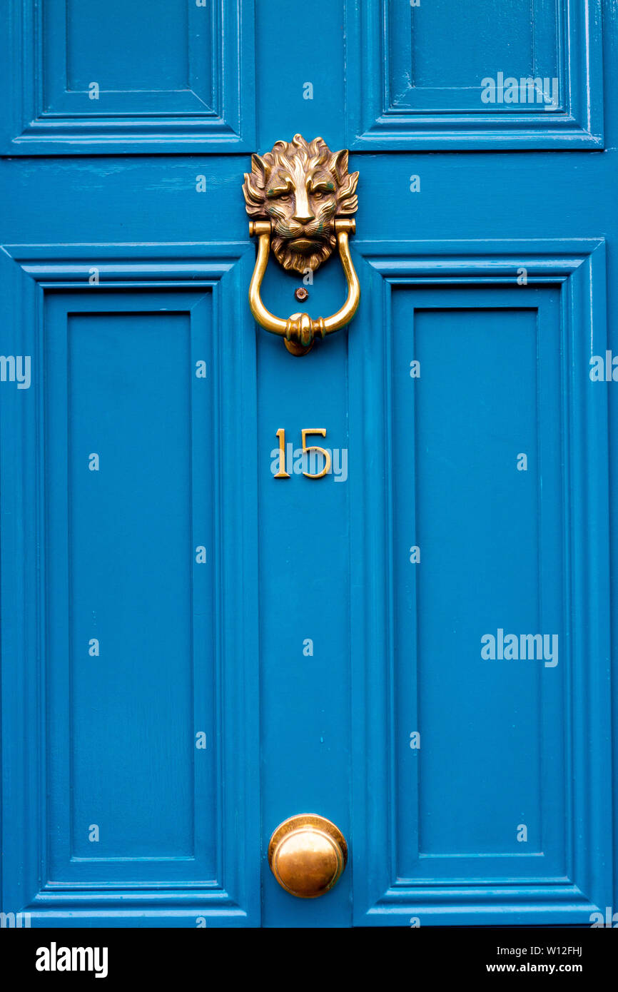 House number fifteen with the 15 in bright yellow on a blue wooden front door and ornate lions head door knocker Stock Photo