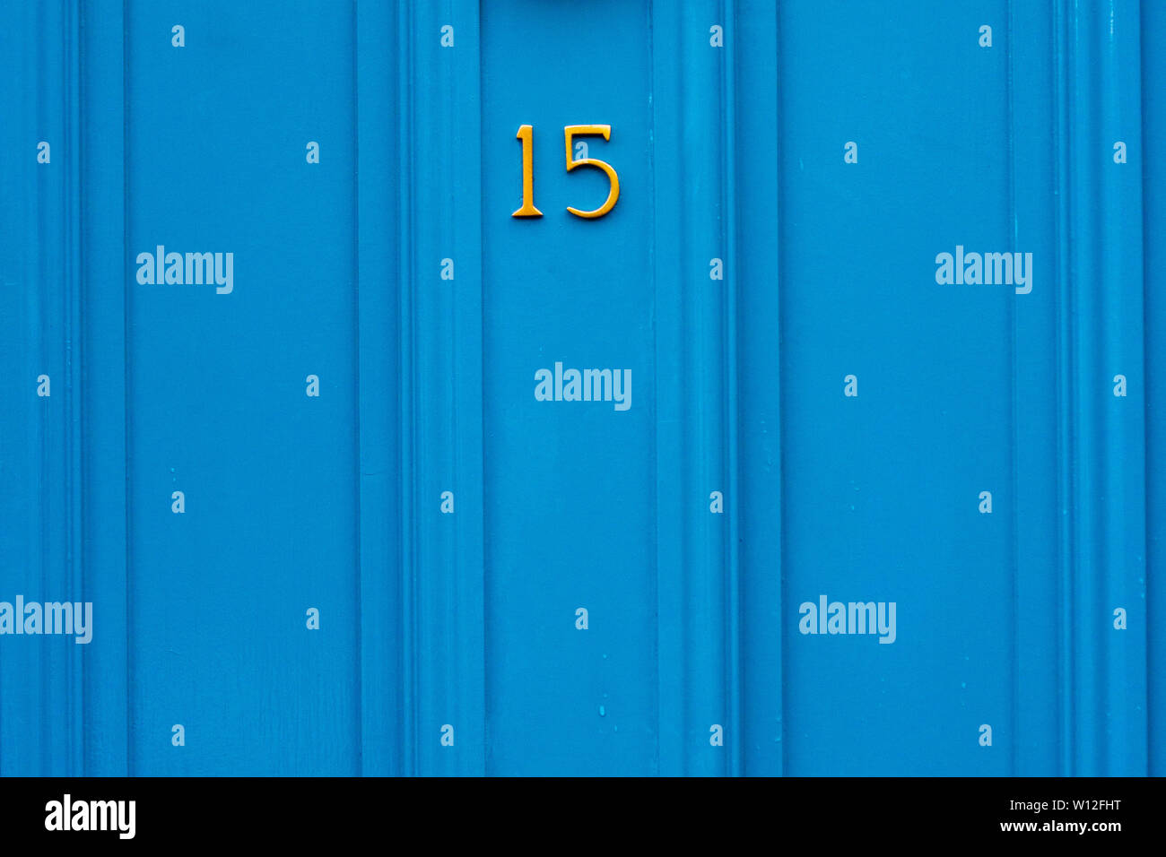 House number fifteen with the 15 in bright yellow on a blue wooden front door Stock Photo