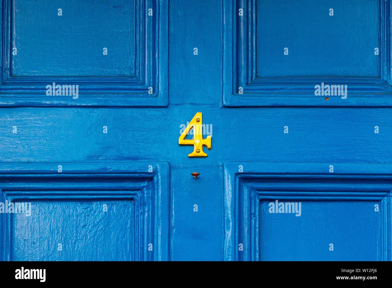 House number four with the 4 in bright yellow on a blue wooden front door Stock Photo