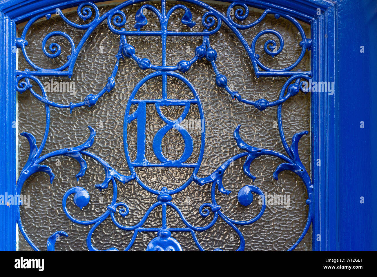 House number 18 worked in elaborate and ornate iron scrollwork on a glass door Stock Photo