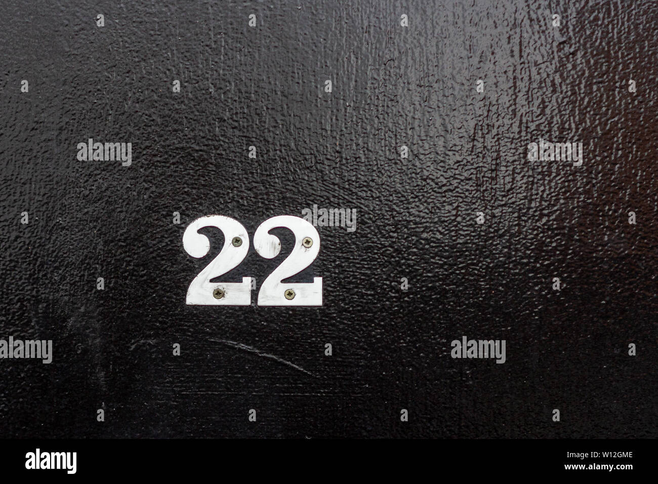 House number 22 with the twenty-two in silver digits on a black wooden front door with peephole Stock Photo