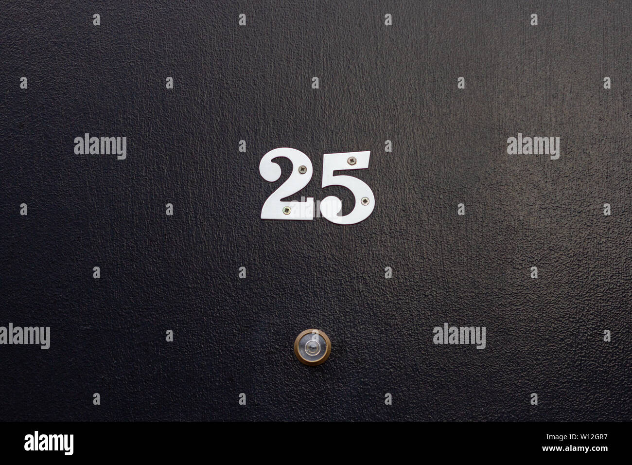 House number 25 with the twenty-five in silver digits on a black wooden front door with peephole Stock Photo
