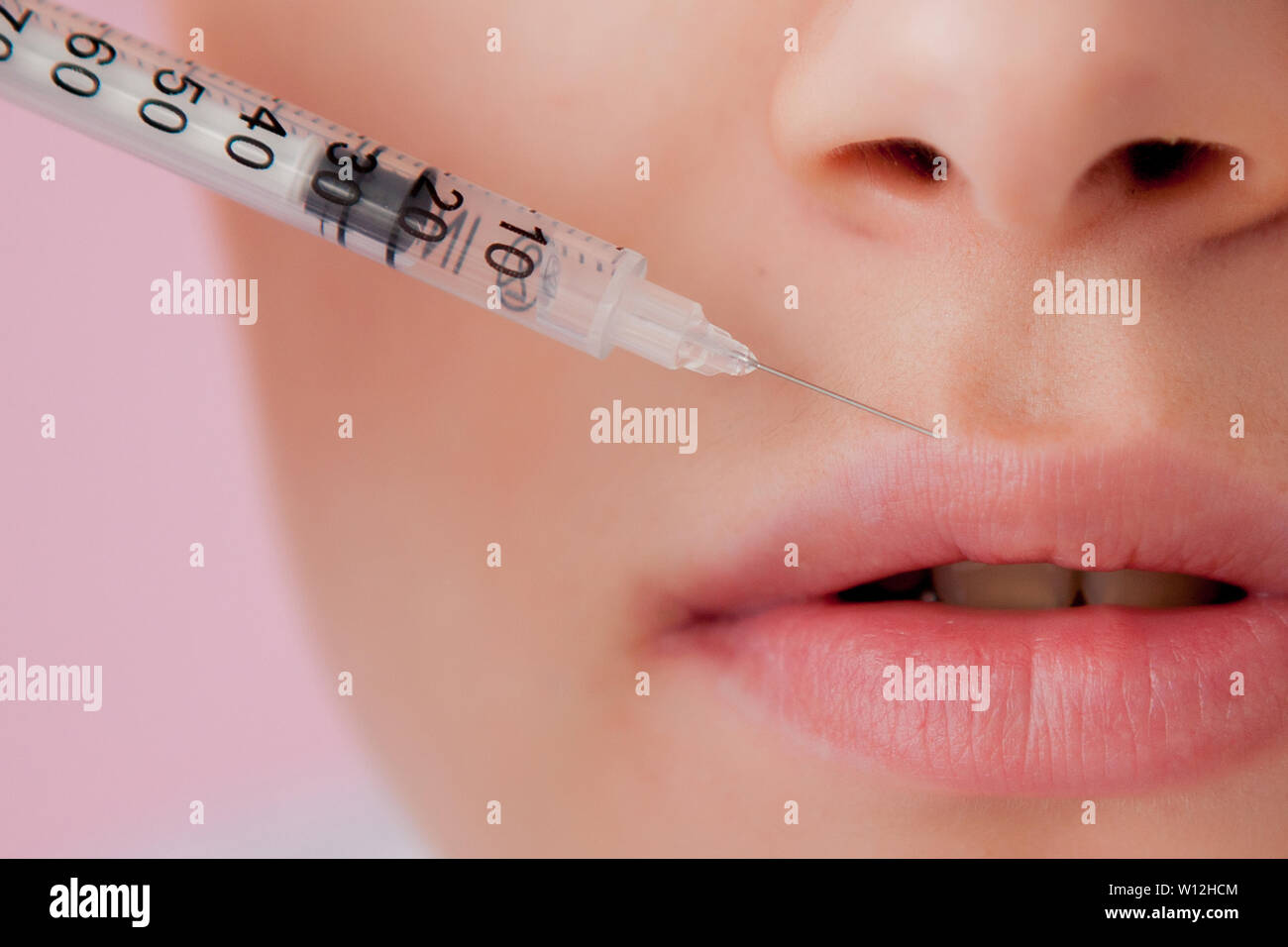 Doctor in gloves giving woman botox injections in lips, on pink ...