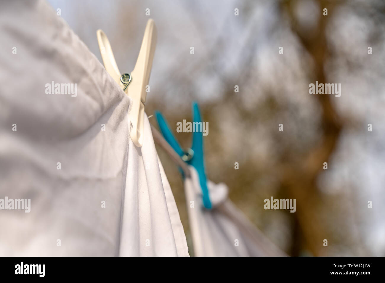 White clothes hung out to dry on a washing line and fastened by the clothes pegs in the bright warm sunny day. Blurred garden at the background. Stock Photo