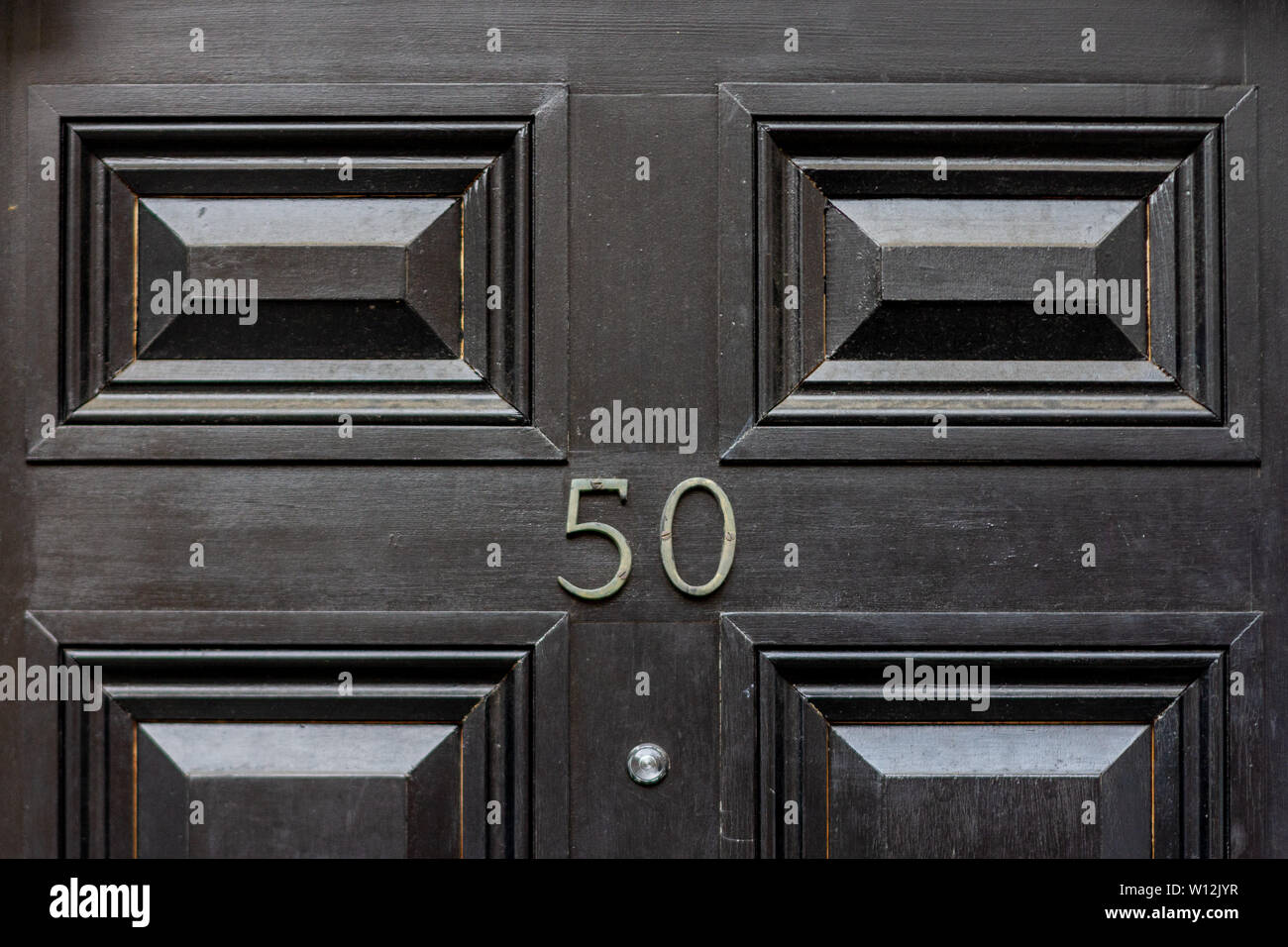House number fifty with the fifty in metal digits on a black painted old wooden front door Stock Photo