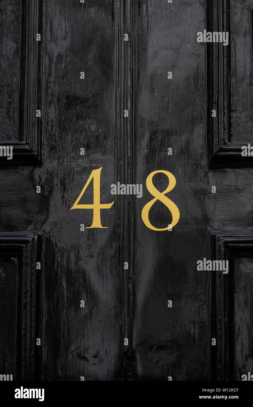 House number 48 with the forty-eight painted in gold on a black painted old wooden front door Stock Photo