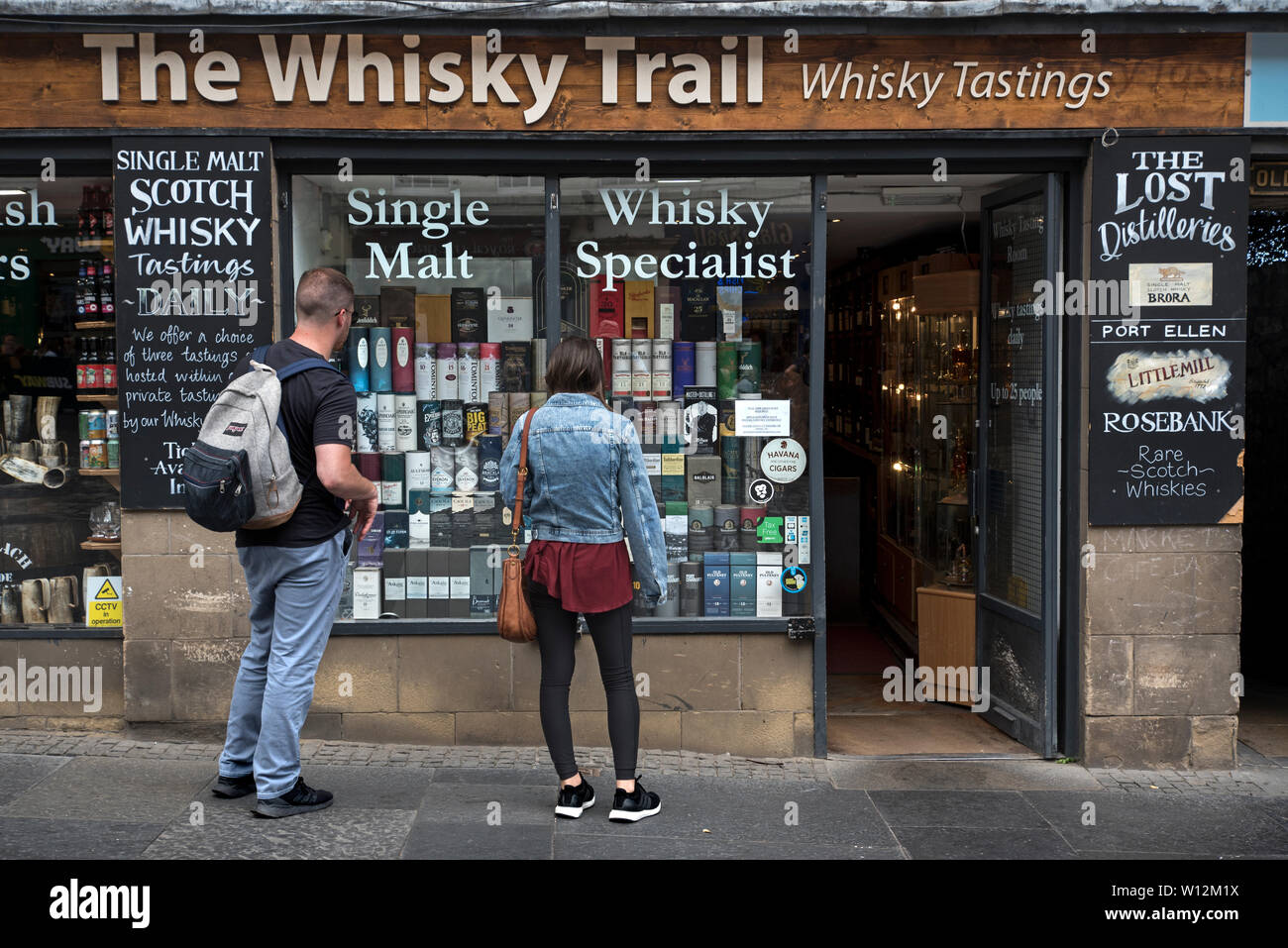 A young couple look into the window of The Whisky Trail shop on the High Street, Edinburgh, Scotland, UK. Stock Photo