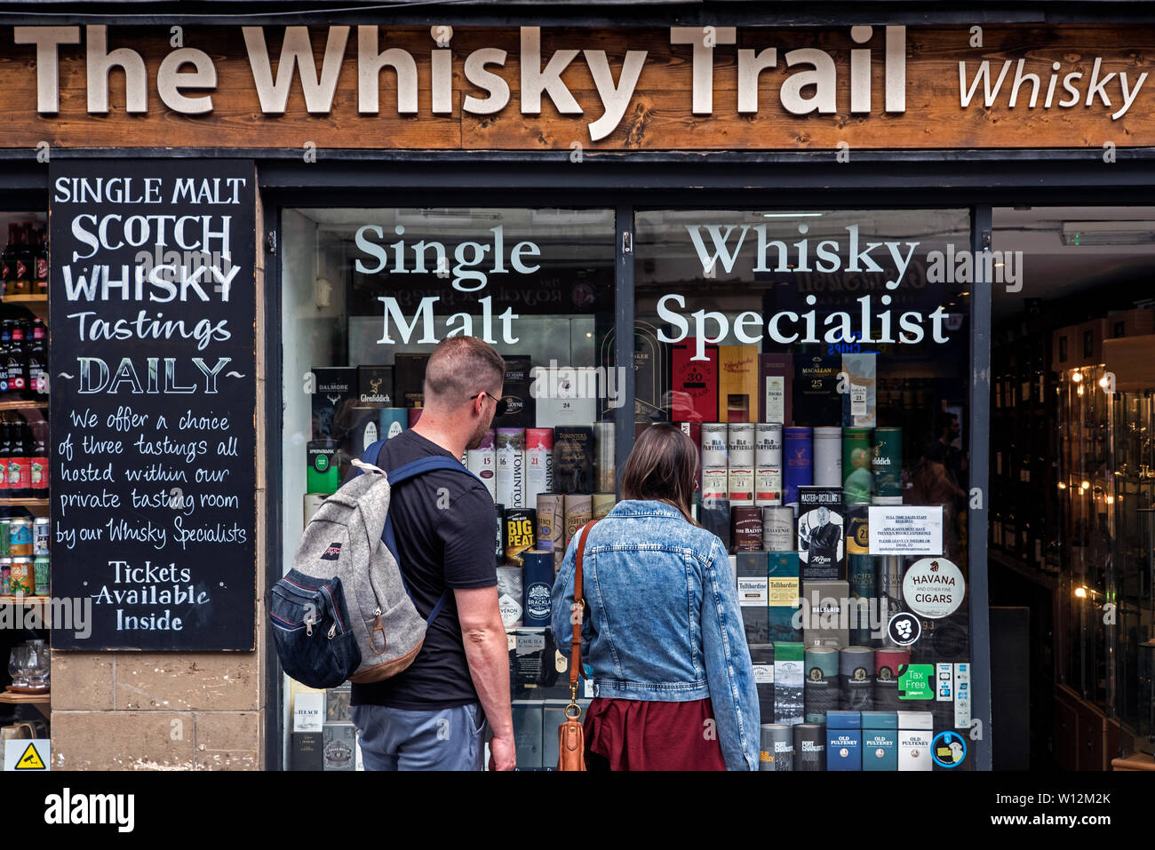 A young couple look into the window of The Whisky Trail shop on the High Street, Edinburgh, Scotland, UK. Stock Photo