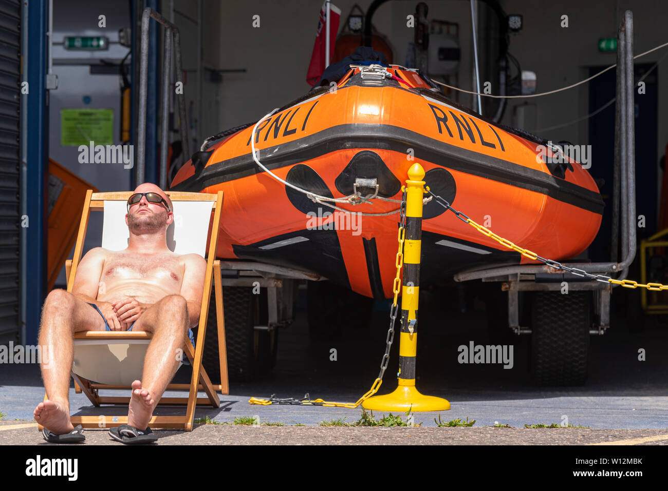 RNLI crew member Dave Cartwright sunbathing during a heatwave outside the boathouse at Southend on Sea, Essex, UK. D class inshore lifeboat Stock Photo