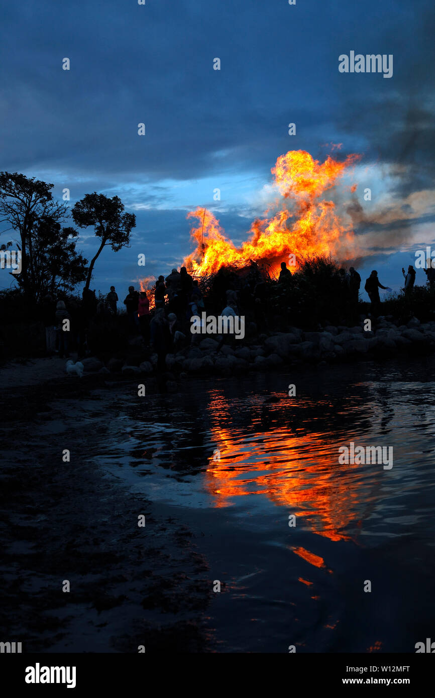 Bonfire on the beach at Nivaa Harbour in celebration of midsummer and St. John's Eve. Flames reflected in the shallow water in the sound Øresund. Stock Photo