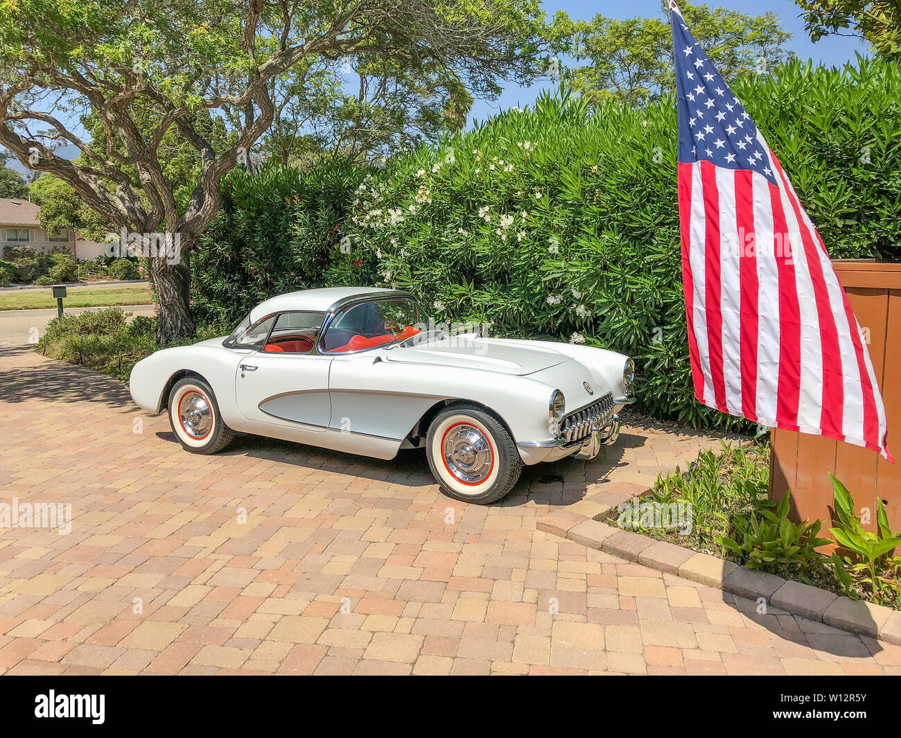 Side view of a  white with silver 1957 Corvette with the optional hardtop with the American flag in front of the car. Stock Photo