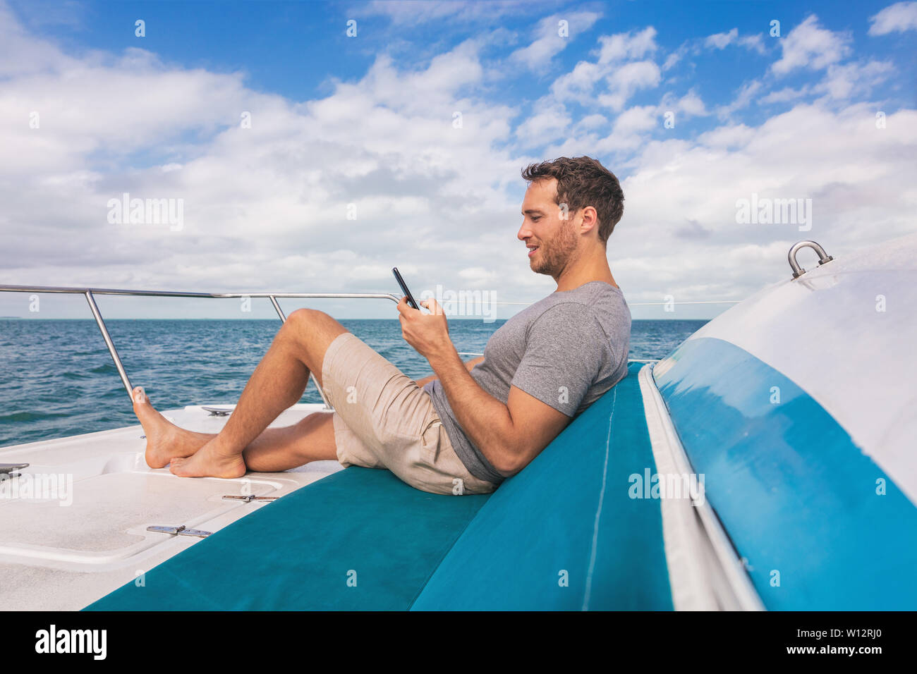 Boat man using mobile phone texting on satellite internet while relaxing on deck of yacht luxury lifestyle. Stock Photo
