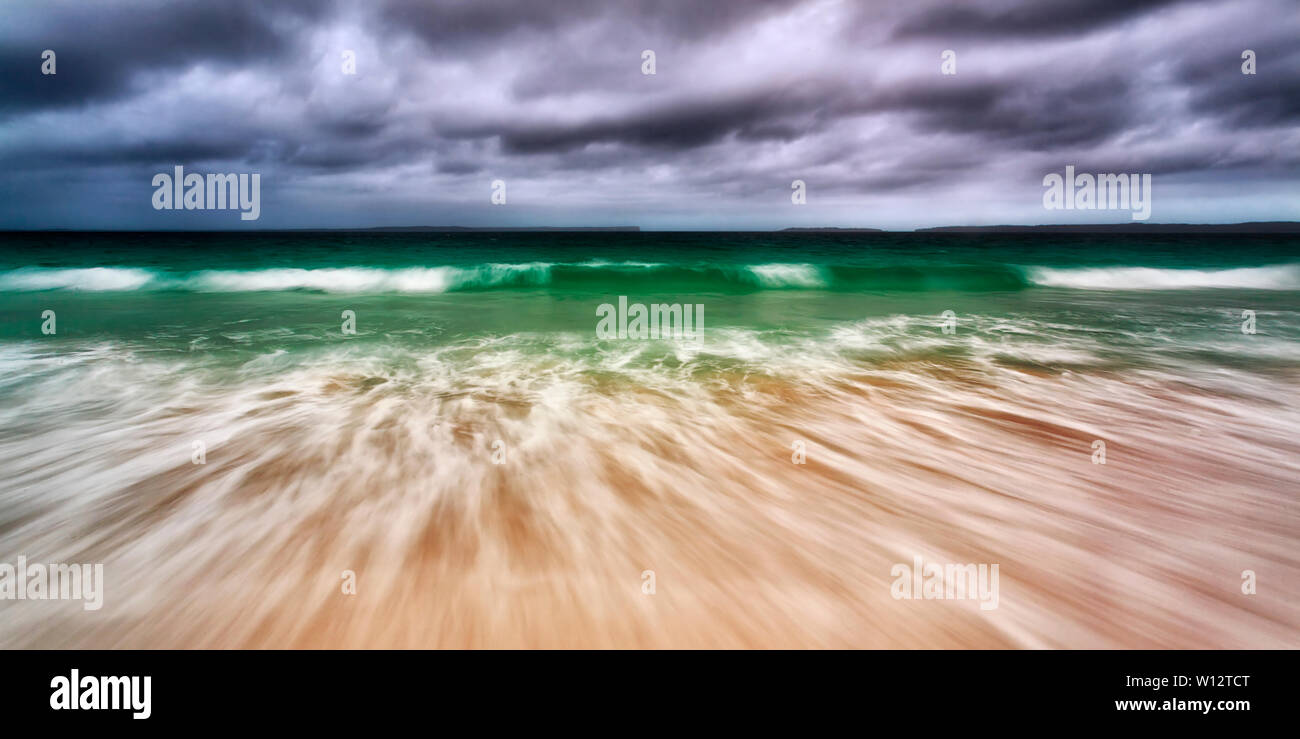 Wide seascape panorama of emerald waves under moody stormy sky rolling on white sand of Jervis bay beach on NSW pacific coast of Australia. Stock Photo