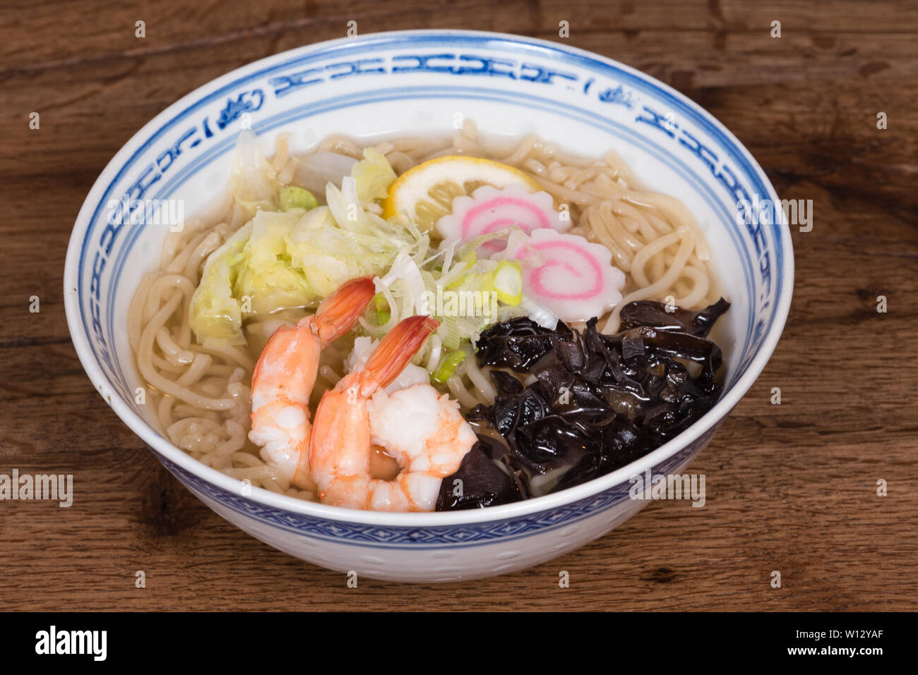 Ramen Shio with fish broth, shrimp, naruto Kamaboko, black mushrooms, Chinese cabbage, dark wood table background Stock Photo