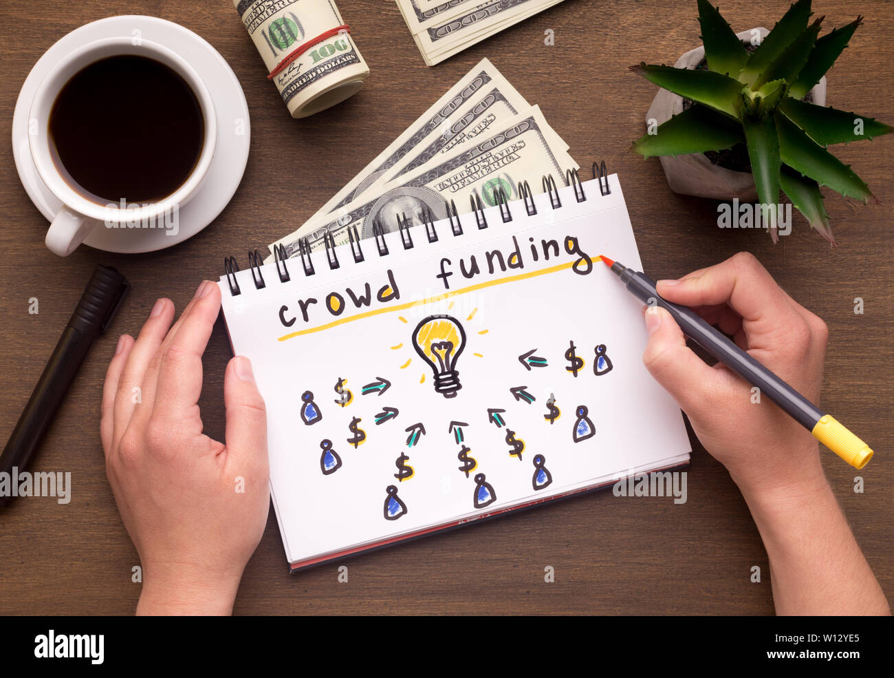 Woman hand writing in notebook crowdfunding sign on table Stock Photo
