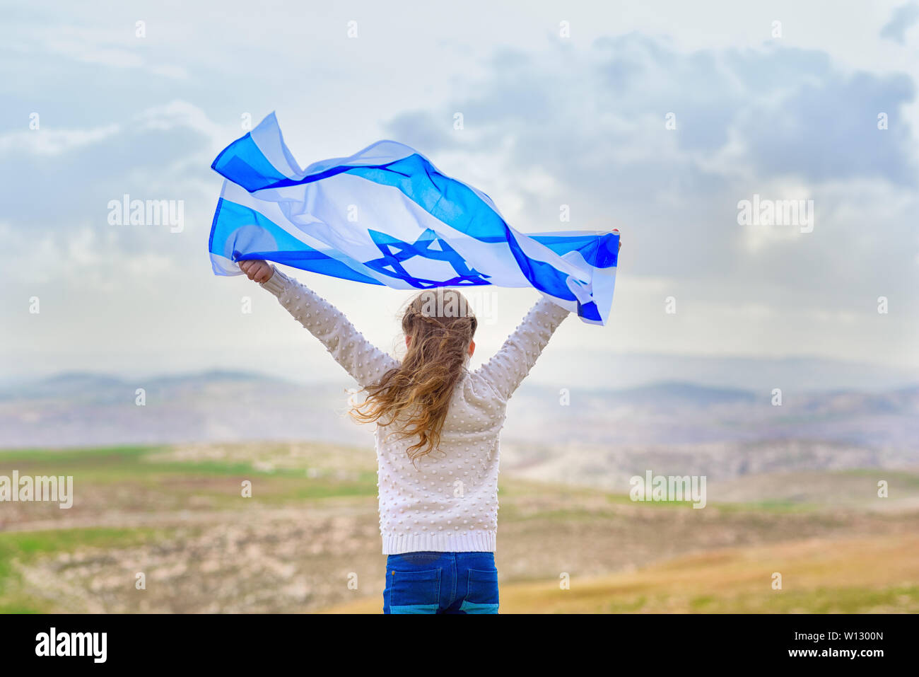 Little patriot Jewish girl standing and enjoying with the flag of Israel on blue sky background. Memorial day-Yom Hazikaron, Patriotic holiday. Stock Photo