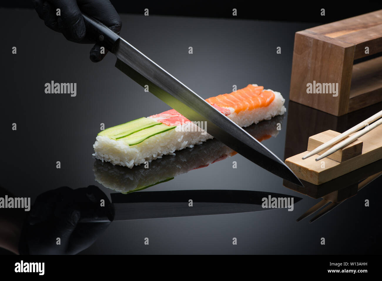 chef prepares sushi, cuts with a knife. sushi on black background with reflection Stock Photo