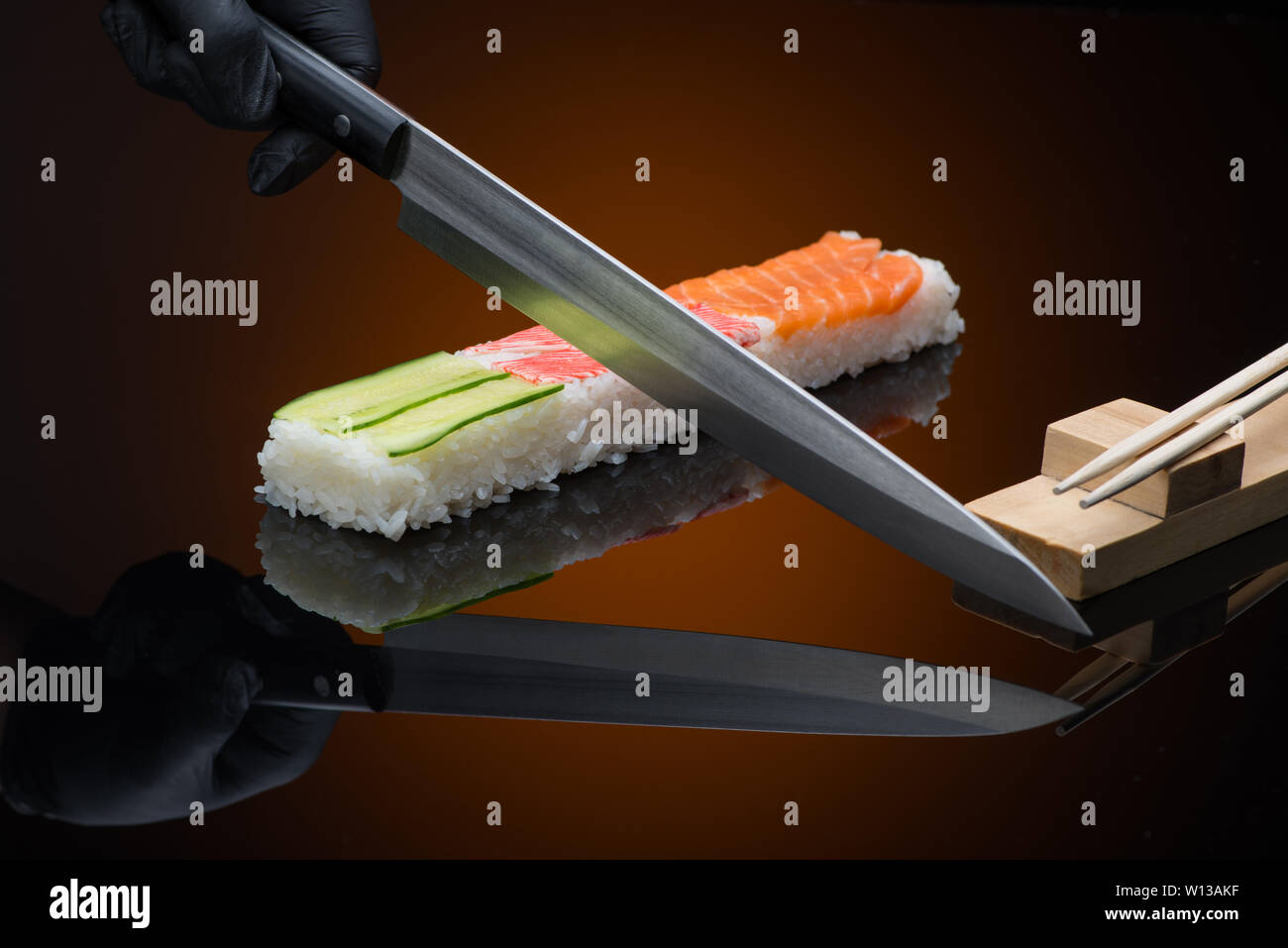 chef prepares sushi, cuts with a knife. sushi on red  background with reflection Stock Photo
