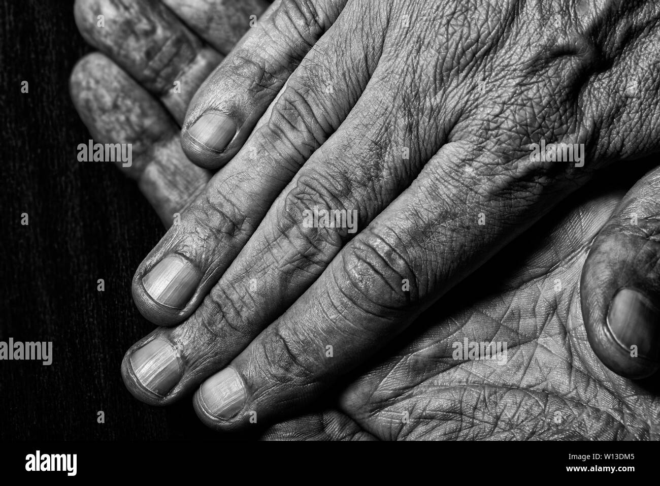 Black and White photo of senior man crossed hands detail on dark background Stock Photo