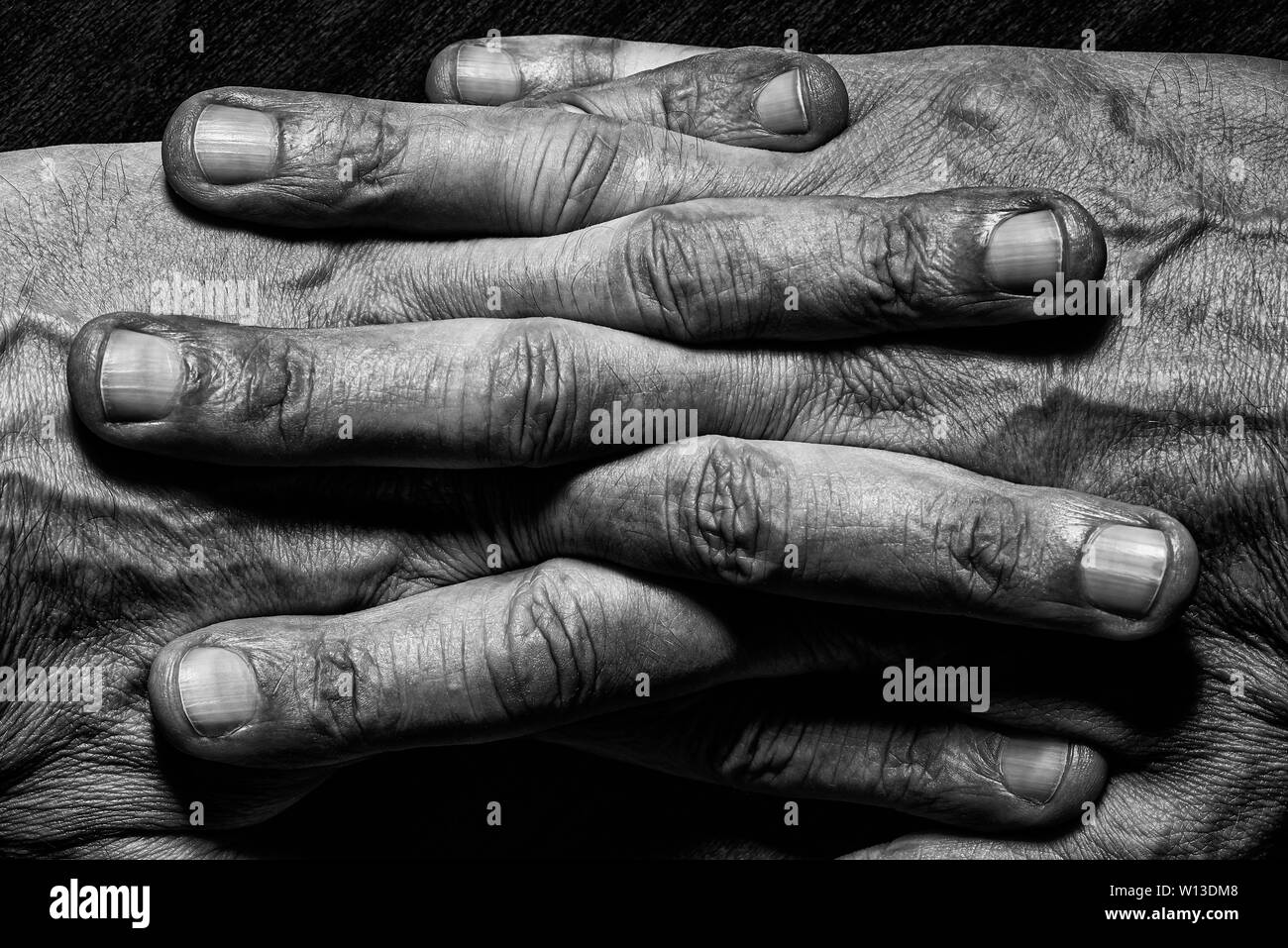 Black and White photo of senior man hands with crossed fingers on dark background Stock Photo